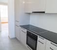Modern kitchen with white cabinets, black countertops, an induction stove, and an oven. The space is bright and clean with tiled flooring.