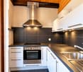 Modern kitchen with white cabinets, stainless steel appliances, dark countertops, and a sleek range hood.