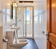 Modern bathroom with white tiles, a toilet, sink, shower, and a large window offering a view of the outdoors.
