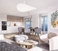 Modern open-plan living and dining area with a view, featuring a white sofa, coffee table, ottoman, dining table with chairs, and a kitchen area with white cabinets and stainless steel appliances.