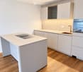 Modern kitchen with light-colored cabinets, a central island with a built-in sink, and a sleek faucet. The space features wooden flooring and built-in lighting above the counter.
