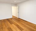Empty room with light wooden flooring and white walls, featuring an open doorway leading to another space.
