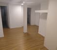 Empty room with wooden flooring and white walls, featuring a central column and doorways leading to other rooms.