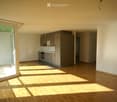 Empty kitchen with wooden flooring, grey cabinets, and a large window letting in natural light.