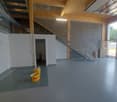 Empty room with concrete floor, white walls, staircase, and a door leading to a small room with a sink.