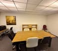 Empty office with a large wooden table, several chairs, and a cabinet. The walls are white, and there is a framed painting on one of the walls.