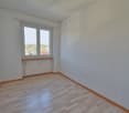 An empty room with a window, radiator, and wooden floor