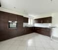 modern kitchen with wooden cabinets, white tiled floor, built-in oven, sink, countertop, window
