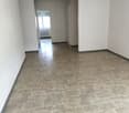Empty room with white walls, gray tile floor, two doors, one with a window, and a radiator.