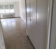 Empty room with wooden floor, white walls, large windows, white radiator, and white wardrobes