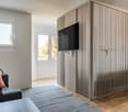 Small room with couch, a table, a mounted television, a window, a lamp, and a curtain.