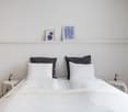 minimalist room with double bed, white bedding, black cushions, bedside tables, and wall art
