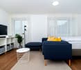 A living room with a bed, sofa, TV, shelf, lamp, and plant