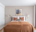 Double bed, white bedding, brown throw, bedside lamps, picture frame, curtains, wardrobe