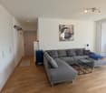 modern living room with gray sectional sofa, wooden floor, white walls, large windows, artwork, side tables, and a rug