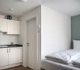 small room with a bed, a sink, a small stove, and a refrigerator