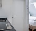kitchen area with sink, induction hob, white walls, white door, bed with white bedding