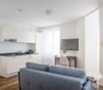 modern kitchen with white cabinets, wooden floor, gray couch, dining table, TV, lamp