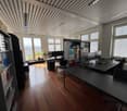 modern office with wooden floor, large windows, desks, chairs, bookshelves, monitors, plants