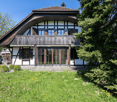 2 story house, brown roof, white walls, wooden balcony, glass doors, large windows, garden