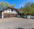 Traditional house with brown roof, white and brown walls, two wooden garages, paved driveway, trees, and plants