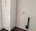 White appliance, likely a washing machine or dryer, with control panel visible. Tiled floor and plain white walls.