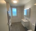 Spacious bathroom with tiled walls, a vanity sink, a toilet, and a washing machine. The room has a large window providing natural light.