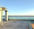 Large outdoor space with tiled floor, glass railing, overlooking sea