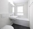 Bathroom: white tiles, white sink, white bathtub, white toilet, mirror, window