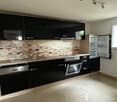 Modern kitchen with black cabinets, stainless steel appliances, and a brick backsplash. The kitchen has a dishwasher and appears to be a spacious and well-designed space.