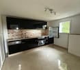 Modern kitchen with black cabinets, stone backsplash, stainless steel appliances including a dishwasher, and tiled flooring.