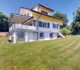 2 story house, yellow exterior, balcony, white windows, tiled roof, garage door, trees, wide lawn