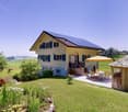 2 story house, yellow exterior, solar panels on the roof, terrace, garden, gazebo, green lawn, dining area with table and chairs, trees
