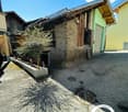 Single-story house with gravel driveway, garage, stone walls, concrete curb, small trees, sunny day