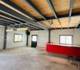 spacious room, metal beams, wooden ceiling, red countertop, black chairs, projector, stairs, windows