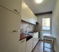 white kitchen cabinets, white refrigerator, white desk, white chair, sink with faucet, brown tiled floor, glass door