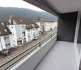 A balcony with a metal railing and a view of a street with parked cars and buildings.