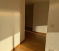 Empty room with wooden floor, white walls, and an open door leading to another room.