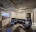 A room with a concrete ceiling, a couch, two armchairs, a window, and a radiator.