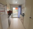 White refrigerator, gas stove, sink, kitchen cabinets, blue curtain, balcony with awning