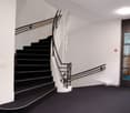 black carpet, white walls, black staircase, metal handrail, glass door
