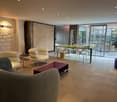 Spacious open-plan living area with comfortable seating, a dining table, and large windows providing natural light. The room features a modern and minimalist design with neutral colors and clean lines.