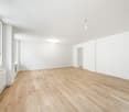 Empty room with wooden floor, white walls, large windows, ceiling lamps