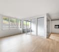 Empty room with large windows, wooden floor, white walls, sliding glass doors leading to balcony.