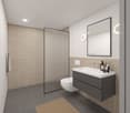 Modern bathroom with grey tiles, beige tiles on wall, glass walk-in shower, white sink, two round wall lights, small rug on the floor, modern toilet.