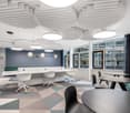 modern conference room, white and blue walls, large windows, geometric carpet, round tables, green couch, modern lighting