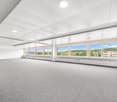 An empty room with gray carpeting, a white ceiling, and large windows offering a scenic view