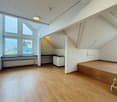 Empty room with wooden floor, white walls, large windows, small kitchen area, and a small raised platform.