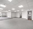 Empty room with white walls, gray carpet, ceiling lights, and a window with a view outside.