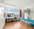 medical office room with desk, chair, medical equipment, examination table, cabinets, window with view